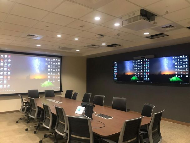 Executive conference room with a long table, ergonomic chairs, projector, and dual monitors