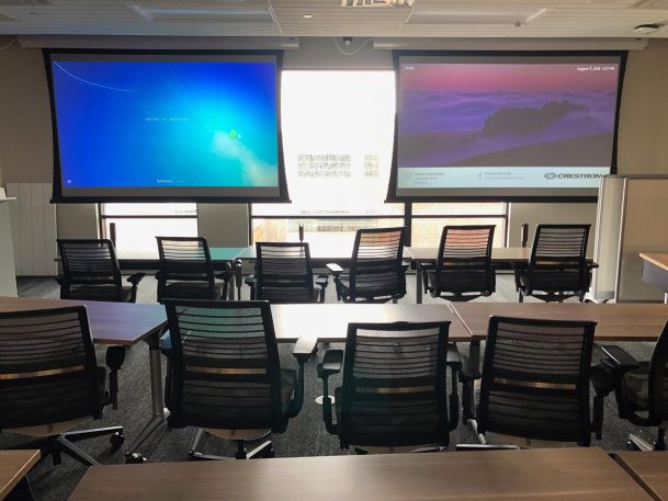 Classroom-style meeting room with black mesh chairs facing dual projection screens