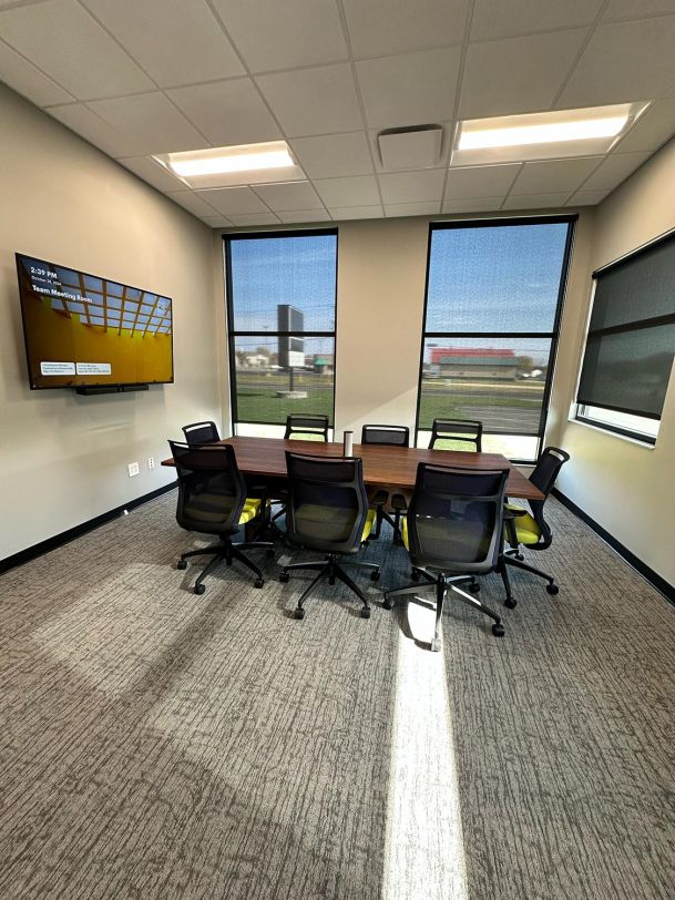 Small conference room with wooden table, mesh chairs, and wall screen
