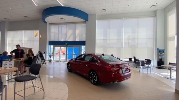 Red sedan parked inside a spacious showroom with large window blinds