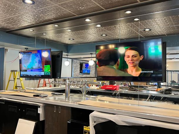 Commercial bar setup featuring multiple suspended television screens above a stainless counter