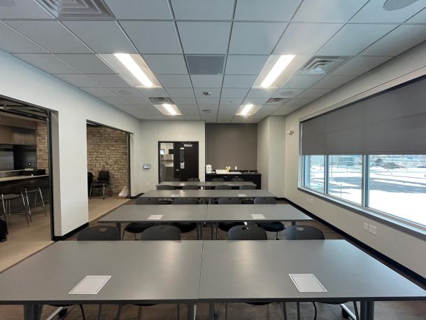 Training room with rows of grey tables, black chairs, and large exterior windows