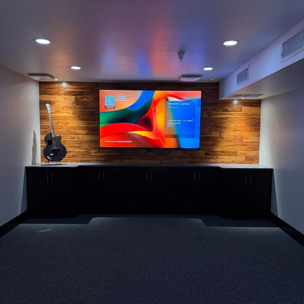 Modern media room featuring a large screen on a wood panel wall and an acoustic guitar