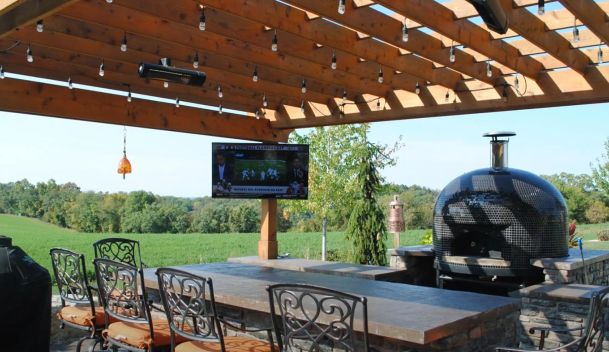 Outdoor patio with wooden pergola, dining counter, pizza oven, and television