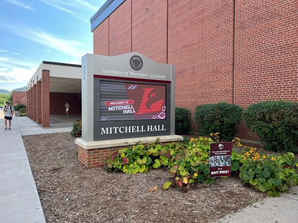 Electronic monument sign surrounded by greenery outside a brick campus building