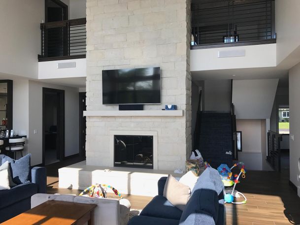 Two-story living room with a stone fireplace, mounted television, and blue sofas