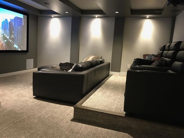 Home theater room with tiered seating, leather sectional sofa, and big screen
