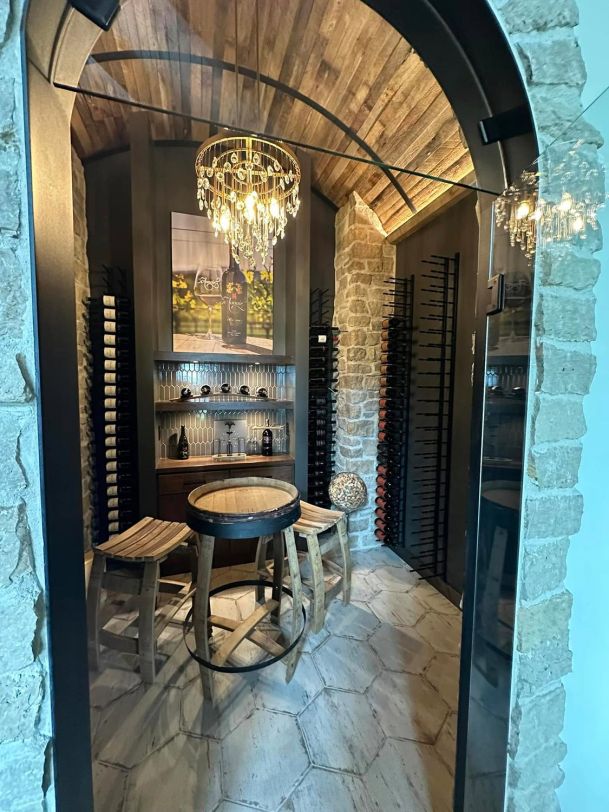 Elegant wine cellar with stone walls, wine racks, chandelier, and barrel table