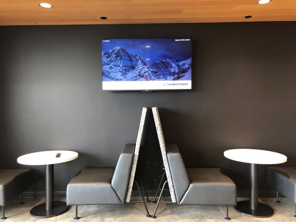 Modern lounge seating area with small round tables beneath a wall-mounted screen
