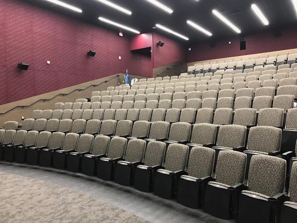 Lecture hall featuring tiered seating with grey cushioned chairs and maroon accent walls