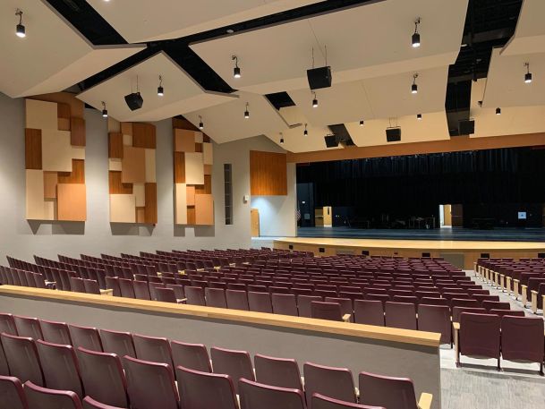Auditorium with rows of maroon seats facing a large stage with ceiling sound panels