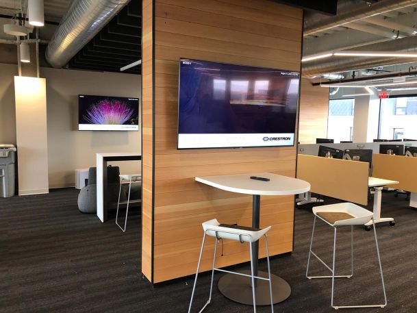 Office collaboration zone featuring a high table with stools next to a wall display