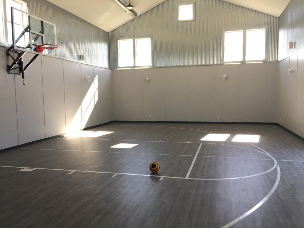 Indoor basketball court with grey flooring, white boundary lines, and a hoop